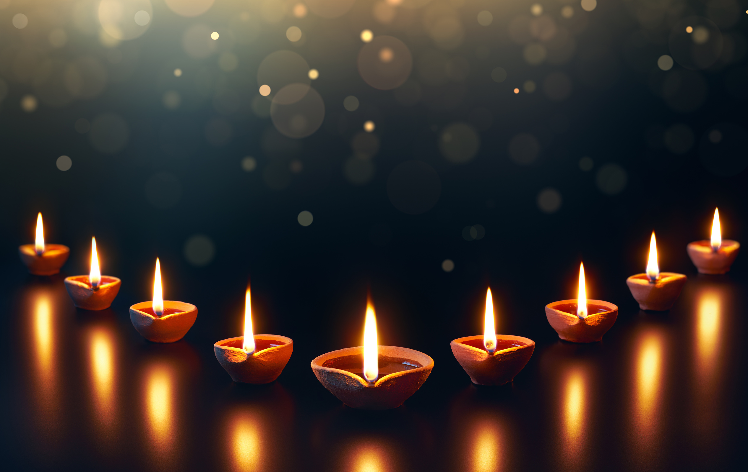 Diya lamps on a reflective base with glittering bokeh